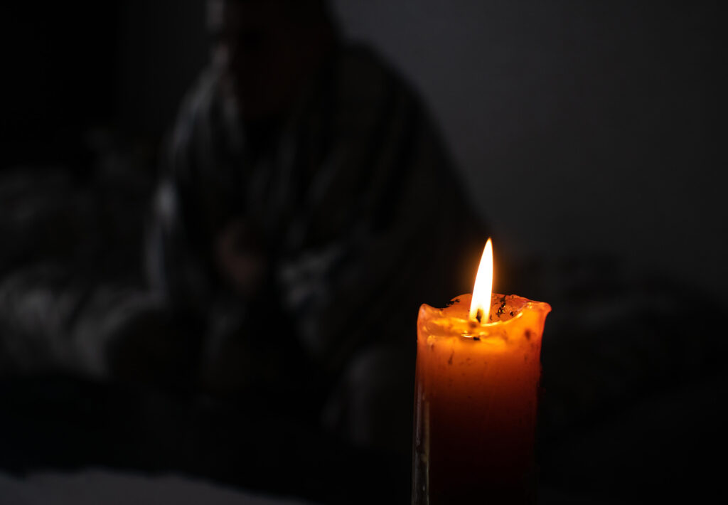 dark room with person in blankets sitting on bed by candlelight